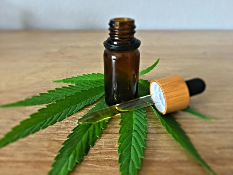 un flacon d'huile CBD ouvert sur une table en bois reposant sur une feuille de marijuana | Justbob