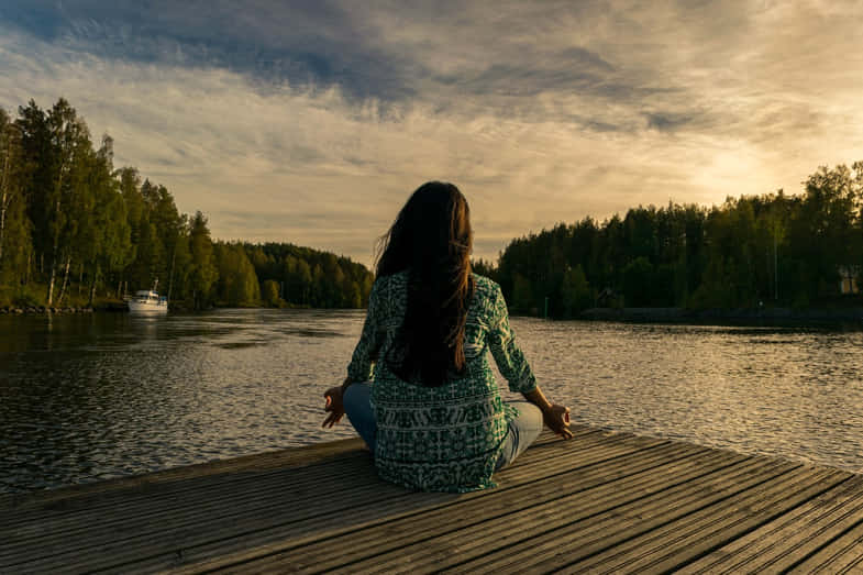 Femme méditant sur la jetée au crépuscule en regardant la mer | Justbob