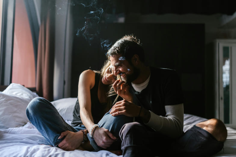 Deux garçons sereins et enlacés fument du cannabis sur le lit | Justbob