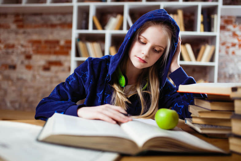 Fille étudiant pour un examen avec de nombreux livres et une pomme verte sur la table | Justbob